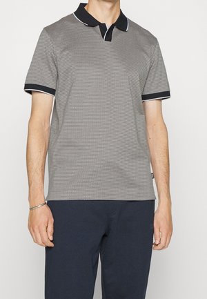 Polo gris texturizado con cuello y puños negros, con un patrón sutil y detalles en azul. Combinado con pantalones oscuros.