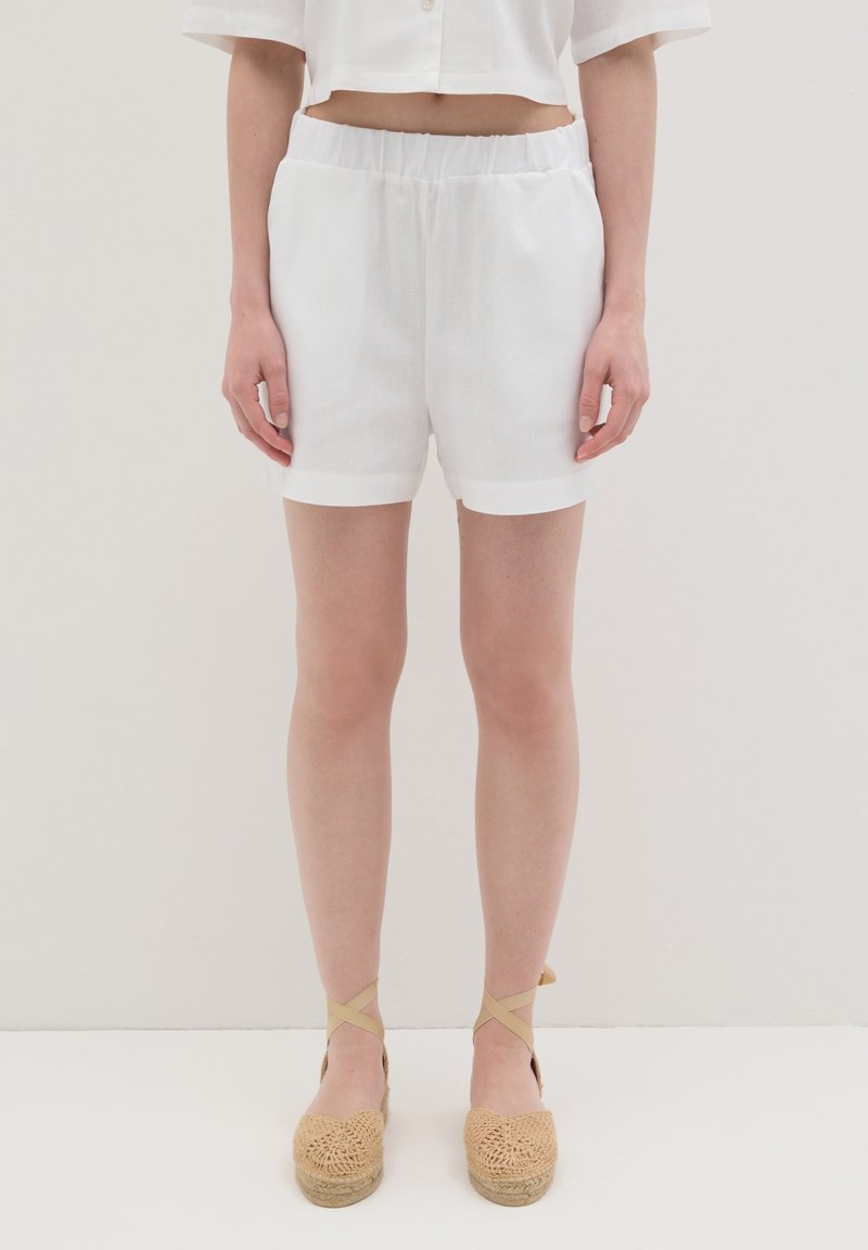 Witte linnen shorts met een elastische tailleband, met een soepele textuur en omgerolde zoom, gecombineerd met geweven tan espadrilles.
