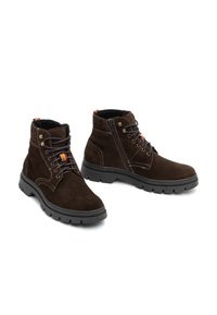Botas de ante marrón hasta el tobillo con diseño de cordones, costuras en contraste y cremallera lateral. Suela de goma negra con superficie texturizada para un mejor agarre.