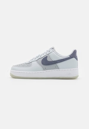 Low-Top-Sneaker in hellgrauen Farbtönen mit einem dunkelgrauen Wildleder-Swoosh und weißer Sohle, seitlich auf weißem Hintergrund gezeigt.