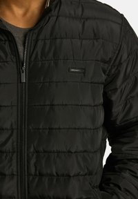 Czarna kurtka puchowa z pikowanym wzorem, zamek błyskawiczny i naszywka z logo. Wykonana z gładkiego, połyskującego materiału z detalami w postaci ribbanu na kołnierzu.