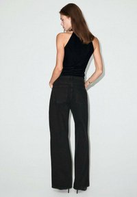 Top negro sin mangas y jeans negros de pierna ancha. El top tiene una silueta ajustada, mientras que los jeans tienen una cintura alta y bolsillos traseros.