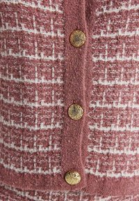 Tissu tricoté texturé rose et blanc avec trois boutons dorés ornés alignés verticalement sur une bande centrale.