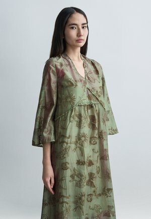 Rochie lungă verde, cu decolteu în V și mâneci trei sferturi. Prezintă modele brodate de diverse forme și detalii texturate de-a lungul tivului.