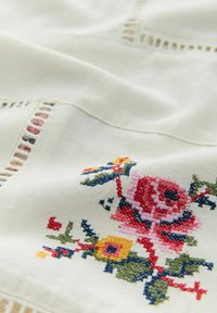 Tessuto ricamato con design floreale in rosa, giallo e verde su uno sfondo crema, caratterizzato da intagli simili a pizzo lungo i bordi.