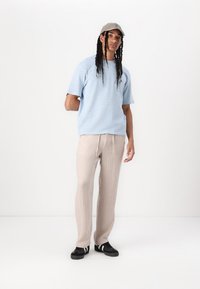 Lyseblå teksturert kortermet skjorte, beige løse bukser og svarte joggesko med hvite detaljer, komplementert med en grå caps.