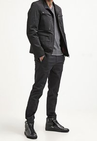 Svart jacka med två dragkedjefickor på bröstet, lagrad över en grå tröja. I kombination med svarta smala byxor och svarta högskurna sneakers.