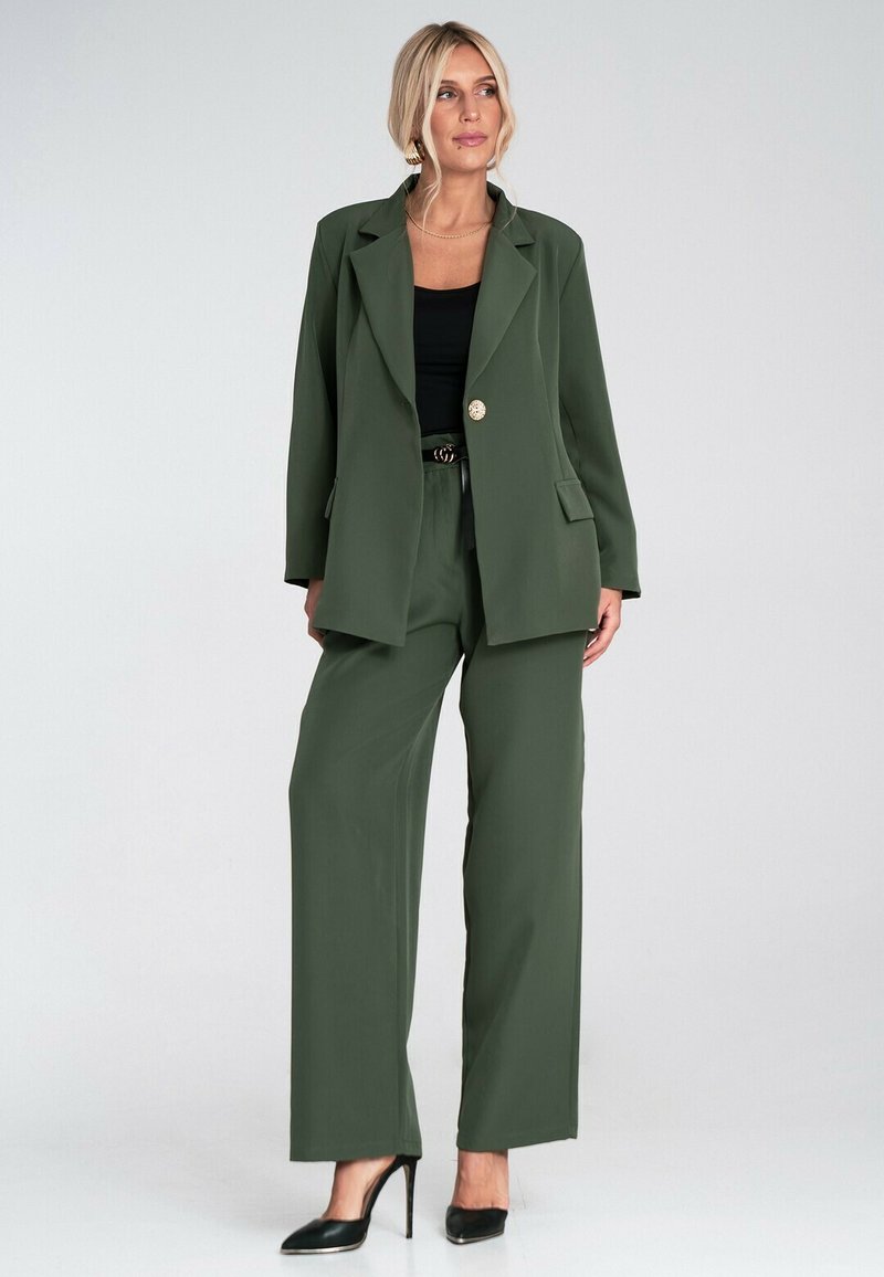 Zielonooliwkowy żakiet o dopasowanym kroju z pojedynczym złotym guzikiem, sparowany z szerokimi spodniami w tym samym kolorze. Teksturowana tkanina o gładkim wykończeniu. Czarny top pod spodem.