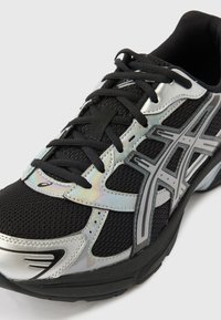 Černá a stříbrná sportovní teniska s prodyšným síťovaným svrchním dílem, černými tkaničkami, reflexními stříbrnými překryvy a vzorovaným šedým logem na boku.