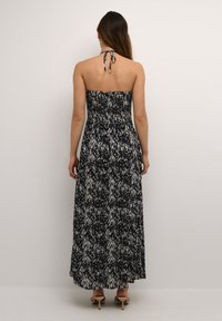 Robe maxi en motif noir et blanc, avec un buste smocké et une attache halter. Le tissu a une texture légère et une silhouette fluide.