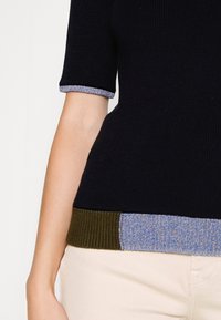 Marineblaues, geripptes Oberteil mit kurzen Ärmeln, das einen blauen und grünen, strukturierten Saum aufweist. Das Design ist figurbetont und hat eine glatte Stoffoberfläche.