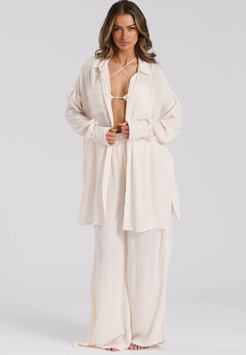 Camicia button-up oversized color beige chiaro con maniche lunghe, abbinata a pantaloni larghi dello stesso colore, in un tessuto strutturato.