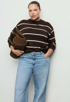 Suéter de rayas marrón, vaqueros azul claro, sosteniendo una bolsa marrón. El suéter tiene una textura acanalada, un ajuste holgado y un diseño de cuello redondo.