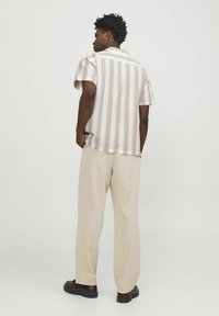 Camisa de manga corta a rayas en color beige claro y blanco de algodón con un corte relajado, combinada con pantalones anchos beige y zapatos oscuros.