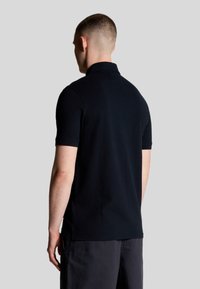 Polo shirt nera con maniche corte, colletto a coste e texture liscia, vista da dietro. Presenta una vestibilità dritta con spacchi laterali.