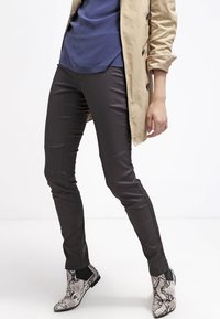 Bruna imitationläderbyxor med smal passform, i kombination med en marinblå topp och svarta och vita ormskinnsmönstrade ankelstövlar. En ljusbeige trench coat bärs.