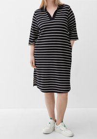 Vestito a righe in bianco e nero con scollo a V e maniche corte; presenta spacchi laterali. Abbinato a sneakers bianche.