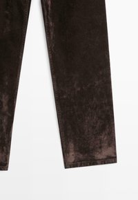 Pantaloni in velluto marrone con texture mostrati dalla metà coscia all'orlo su sfondo bianco.