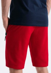 Rode katoenen shorts met een relaxte fit, voorzien van een zijzak en een zwarte ritssluiting, gecombineerd met een marineblauwe T-shirt.