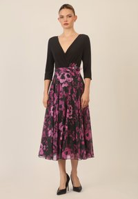 Musta mekko V-aukkolla, kolmella neljänneksellä hihoilla ja istuvalla vartalonmyötäisellä yläosalla. Valuvia hame, jossa on violetti kukkakuosi ja vastaava kangaskukkainen koriste vyötäröllä.