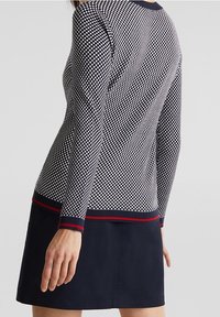 Sweter dzianinowy w kratkę w kolorze granatowym i białym, z jednostajnym granatowym wykończeniem i czerwonymi akcentami, z długimi rękawami i dopasowanym krojem.