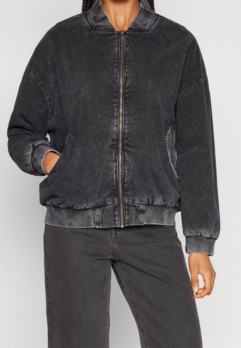 Veste bomber en denim noir avec fermeture éclair à l'avant, poignets et ourlet côtelés. Comprend des poches latérales et une finition légèrement texturée.