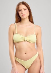 Yellow ribbed bikini featuring a bandeau top with a knotted detail in the center and low-rise bottom with matching texture.