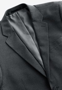 Veste de costume homme gris foncé avec revers à cran, boutonnière visible, un bouton noir et doublure intérieure gris clair.
