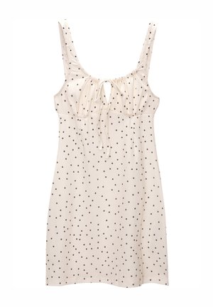 Robe beige clair à pois noirs, avec un col en rond, un détail de lien ajustable et de fines bretelles. Tissu texturé.