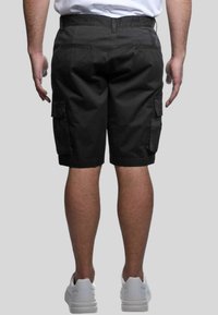Pantaloni cargo neri in cotone con due tasche laterali e una tasca posteriore, rifiniti con un orlo appena sopra il ginocchio. Indossati con sneaker bianche.