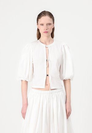 White fitted blouse with puff sleeves, featuring a round neckline and silver hardware closure at the front. Textured fabric with a smooth finish.