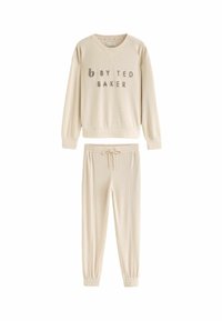 Beige ribakreemides loungewear komplekt, mis sisaldab V-kaelusega sviitrit, millel on tekst "by Ted Baker", ja sobivaid elastse vöökohtadega pükse.