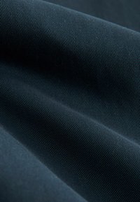 Tissu bleu foncé avec une texture lisse et un motif à rayures fines, affichant un subtil éclat et des plis drapés.