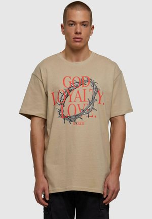 T-shirt oversize beige in cotone, con un design grafico che presenta la scritta rossa "DIO LEALTÀ AMORE" e un'illustrazione di una corona di spine.