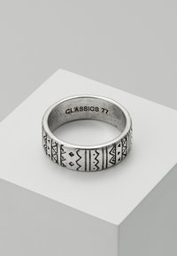 Sølvring med geometriske mønstre graverte rundt ringen, med en teksturert overflate og en innvendig gravering av "CLASSICS 77."