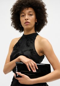 Melnas patentētas ādas piegccilvēku somiņa ar gludu, spīdīgu tekstūru. Tam ir elegants taisnstūra formas dizains un zelta akcenta līnija priekšpusē.