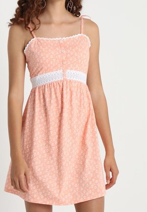 Lichtroze zomerjurkje met witte bloemenpatronen, verstelbare spaghettibandjes, een taille met kanten details en een knoopsluiting aan de voorkant.