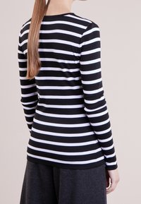 Långärmad topp med svartvita horisontella ränder, tillverkad av elastisk textil, med rund halsringning och åtsittande silhuett.