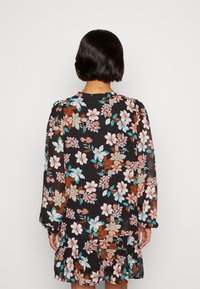 Robe noire à fleurs avec de grandes fleurs roses et bleues, manches longues, ourlet à volants et tissu léger et fluide.