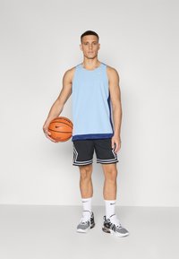 Lyseblå mesh tanktop med marineblå sidepanel, svarte shorts med hvite striper, hvite sokker og svarte joggesko. Holder en oransje basketball.