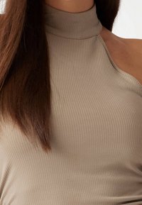 Beige žebrovaný top bez rukávů s vysokým výstřihem a asymetrickým designem ramene, s hladkou textura a přiléhavým střihem.