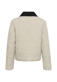 Giacca trapuntata di un beige chiaro con un colletto in velluto a coste nero. Presenta una vestibilità ampia e un motivo di cucitura diagonale sul retro. Maniche lunghe.