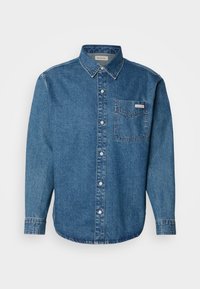 Camisa de denim azul de manga larga con cuello abotonado, bolsillo en el pecho y costuras en contraste. La textura de la tela es suave y tiene un estilo casual.