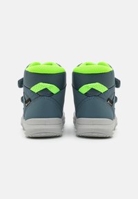 Zapatillas infantiles azules con un diseño texturizado, acentos de malla verde en el cuello y correas de Velcro. Suelas de goma grises con patrones de agarre.