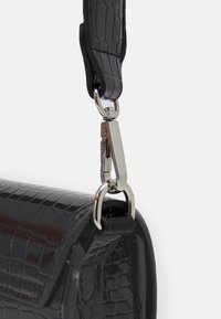 Borsa nera in pelle stampata coccodrillo con tracolla in metallo argentato rimovibile, caratterizzata da una finitura lucida e una superficie testurizzata.