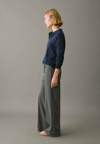 Suéter de punto azul marino con cuello, combinado con pantalones anchos grises y calzado rosa claro, sobre un fondo gris neutro.