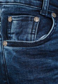 Tmavě modré džíny z denimu s malou přední kapsou s kovovými stříbrnými detaily a kontrastním prošitím. Hladká textura a klasický design.