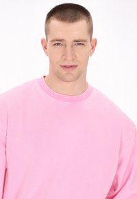Felpa rosa con collo tondo classico e maniche lunghe. Tessuto morbido e liscio con vestibilità rilassata, caratterizzata da un design a tinta unita.