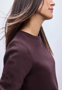 Felpa viola scuro con scollatura rotonda e dettagli a coste, caratterizzata da una texture liscia e una vestibilità ampia, mostrata da un'angolazione laterale.
