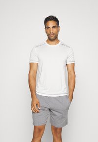 Hvit idretts T-skjorte med korte ermer, rund hals og kontrastsøm, kombinert med grå shorts med snor i livet.